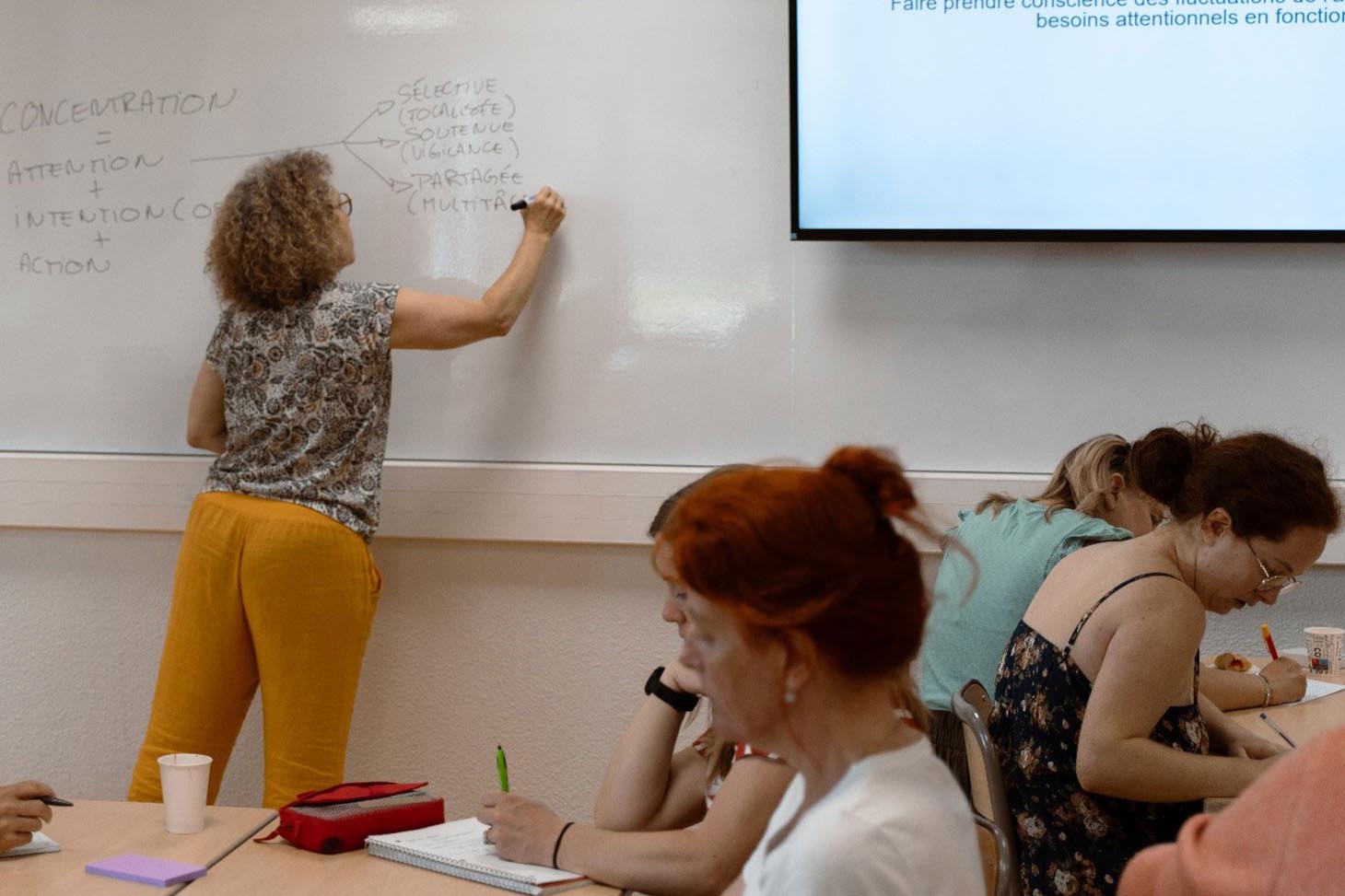 Photo d'une enseignante qui écrit qur un tableau blanc